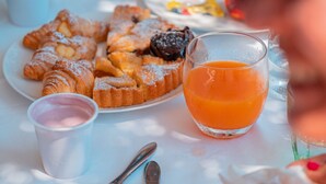 Ein Frühstückstisch mit Gebäck, einem Glas Orangensaft und einer kleinen Tasse Joghurt.