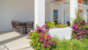 Eine Terrasse im Freien mit Tisch und Stühlen, umgeben von Kübelpflanzen und Blumen.