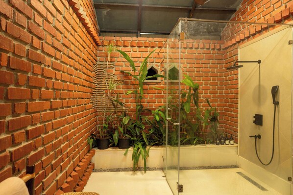 A bathroom with a brick wall, a glass shower enclosure, and potted plants.