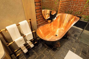Un baño con una bañera de cobre, un perchero de madera y una pared de ladrillo.