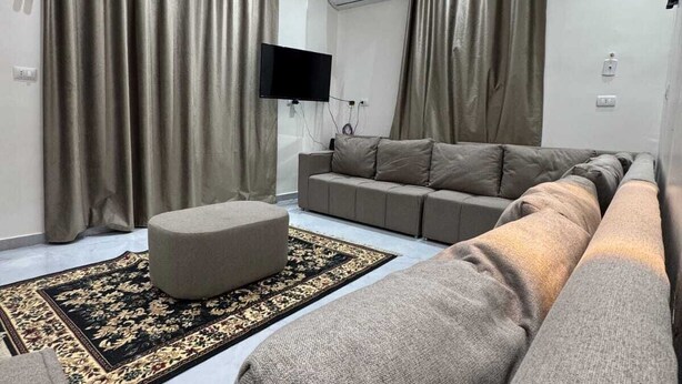 A modern living room with a sofa, ottoman, and a flat-screen TV mounted on the wall. - BEPY'S NUBAIN HOUSE  (Aswan)