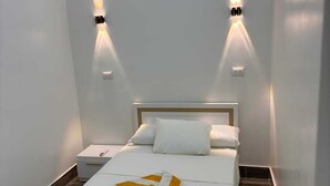 A modern bedroom with a bed, white bedding, and two wall-mounted lights. - BEPY'S NUBAIN HOUSE  (Aswan)