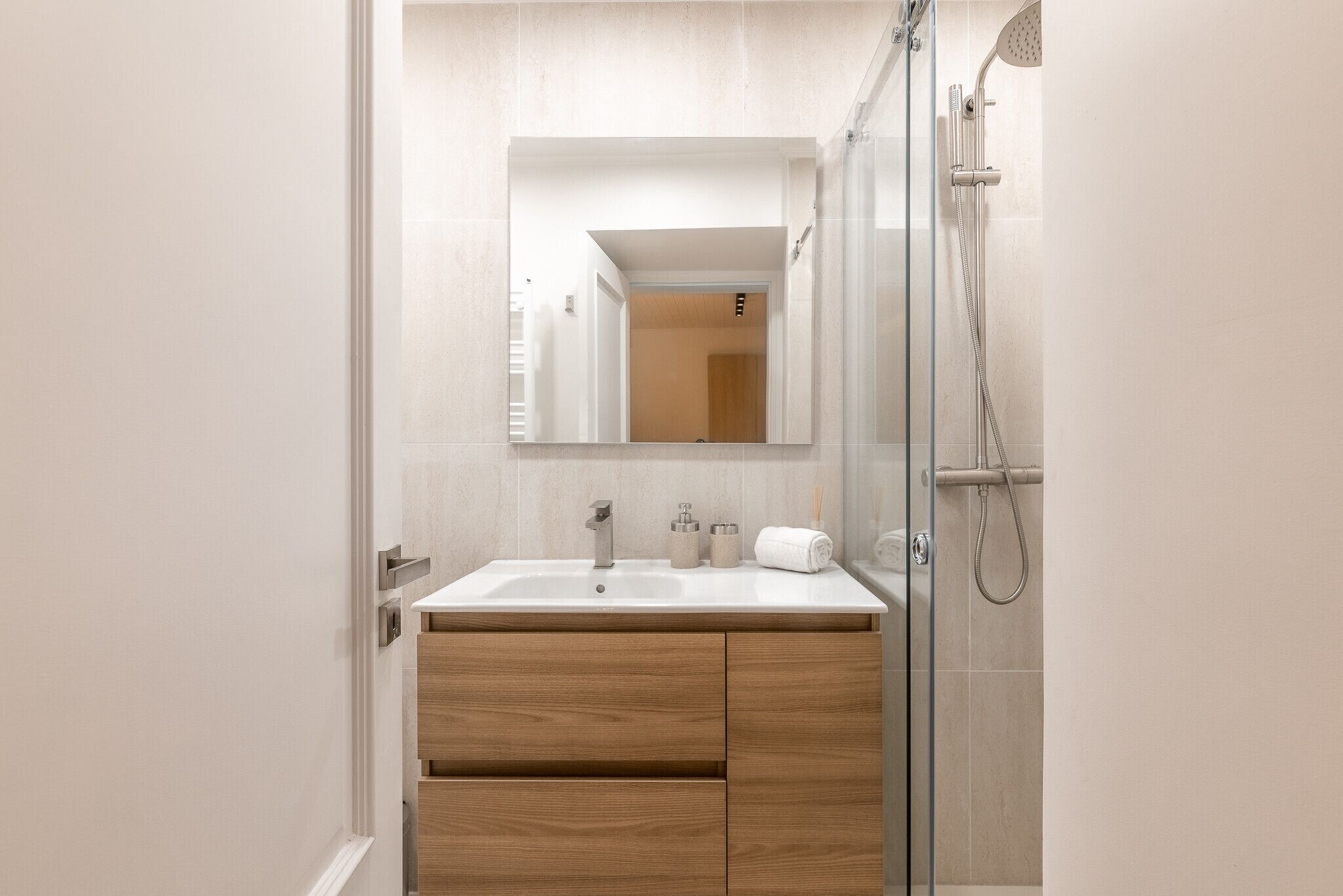 Un bagno moderno con box doccia in vetro, lavandino bianco e mobili contenitori in legno.