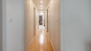 A narrow hallway with wooden flooring and white walls, leading to a room with a bed and a door at the end. - BE Fully Renovated | Central | Private Patio (Lisboa ciudad)
