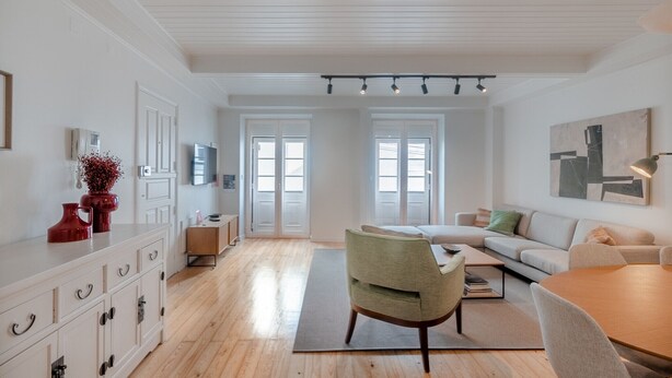 A spacious living area with a wooden floor, a sofa, a dining table, and a kitchen area with white cabinetry and a red vase. - BE Fully Renovated | Central | Private Patio (Lisboa ciudad)