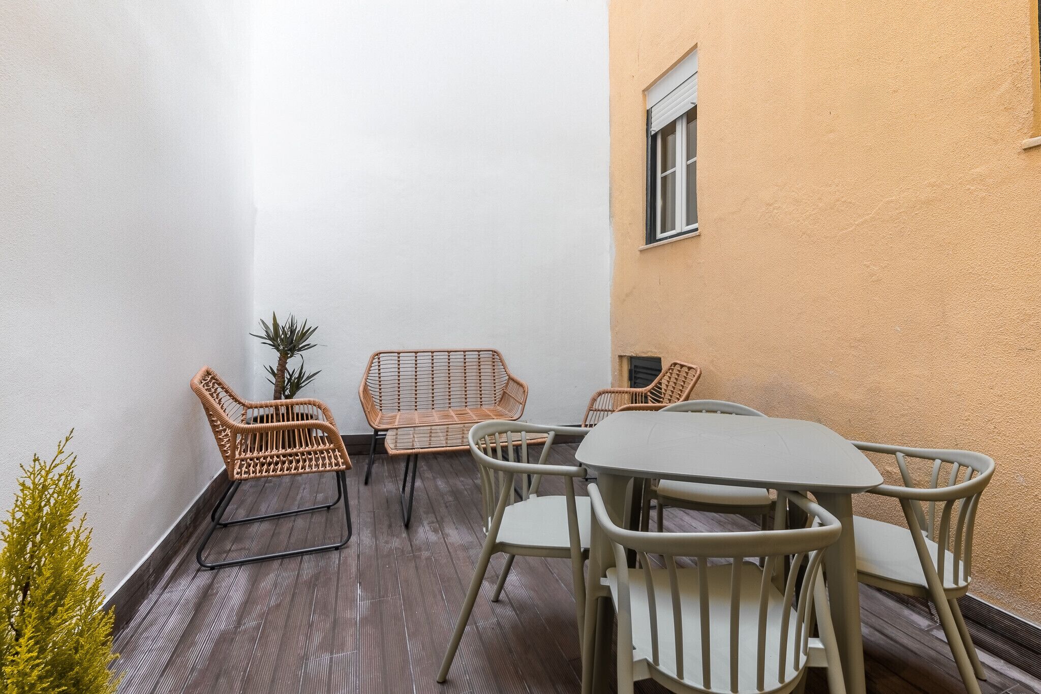 A small patio with a round table and four chairs, a potted plant, and a window.
