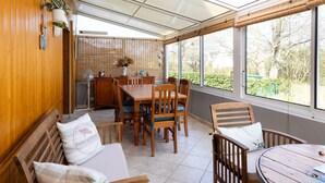 A sunroom with a wooden interior, a dining table, chairs, a bench, and a view of the garden through large windows. - Holiday Home 'L'escale Kénanaise' with Private Garden and Wi-Fi (Saint-Quay-Perros)