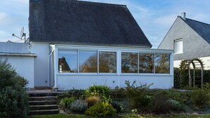 A white house with a large windowed extension, a chimney, and a garden with various plants. - Holiday Home 'L'escale Kénanaise' with Private Garden and Wi-Fi (Saint-Quay-Perros)