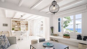 A bright, airy living room with a dining area, large windows with ocean views, and a modern chandelier. - Villa Tiche with private pool - My Rental Homes (Mykonos)