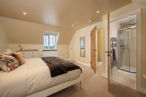 Ein Schlafzimmer mit Bett, Nachttisch, Fenster, einer Tür zu einem Duschbereich und einem Heizkörper.