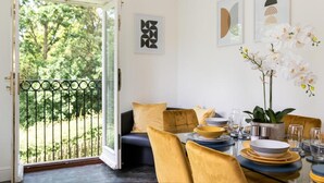A dining area with a table set for four, a sofa with yellow cushions, and a view of greenery through a glass door. - Contractors/family - Parking - Wifi - Sleeps 6 (Milton Keynes)