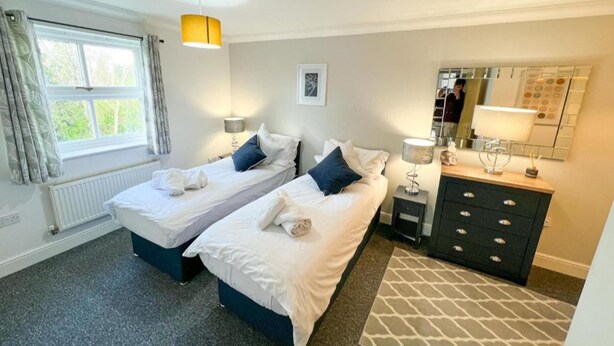 A hotel room with two beds, a large window, a radiator, a mirror, and a dresser. - Contractors/family - Parking - Wifi - Sleeps 6 (Milton Keynes)