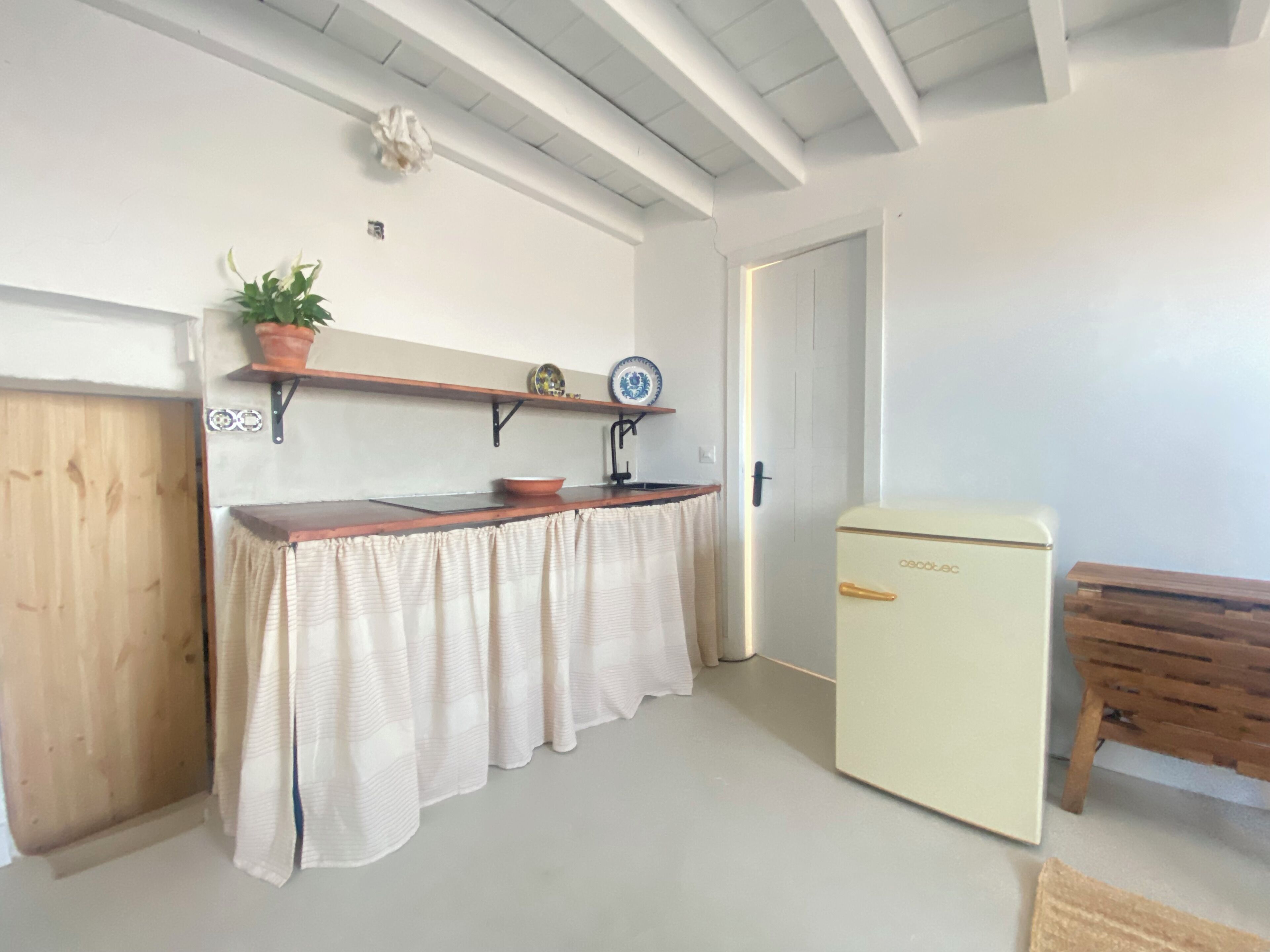 Una piccola cucina con un bancone in legno, un lavandino bianco e un frigorifero vintage.
