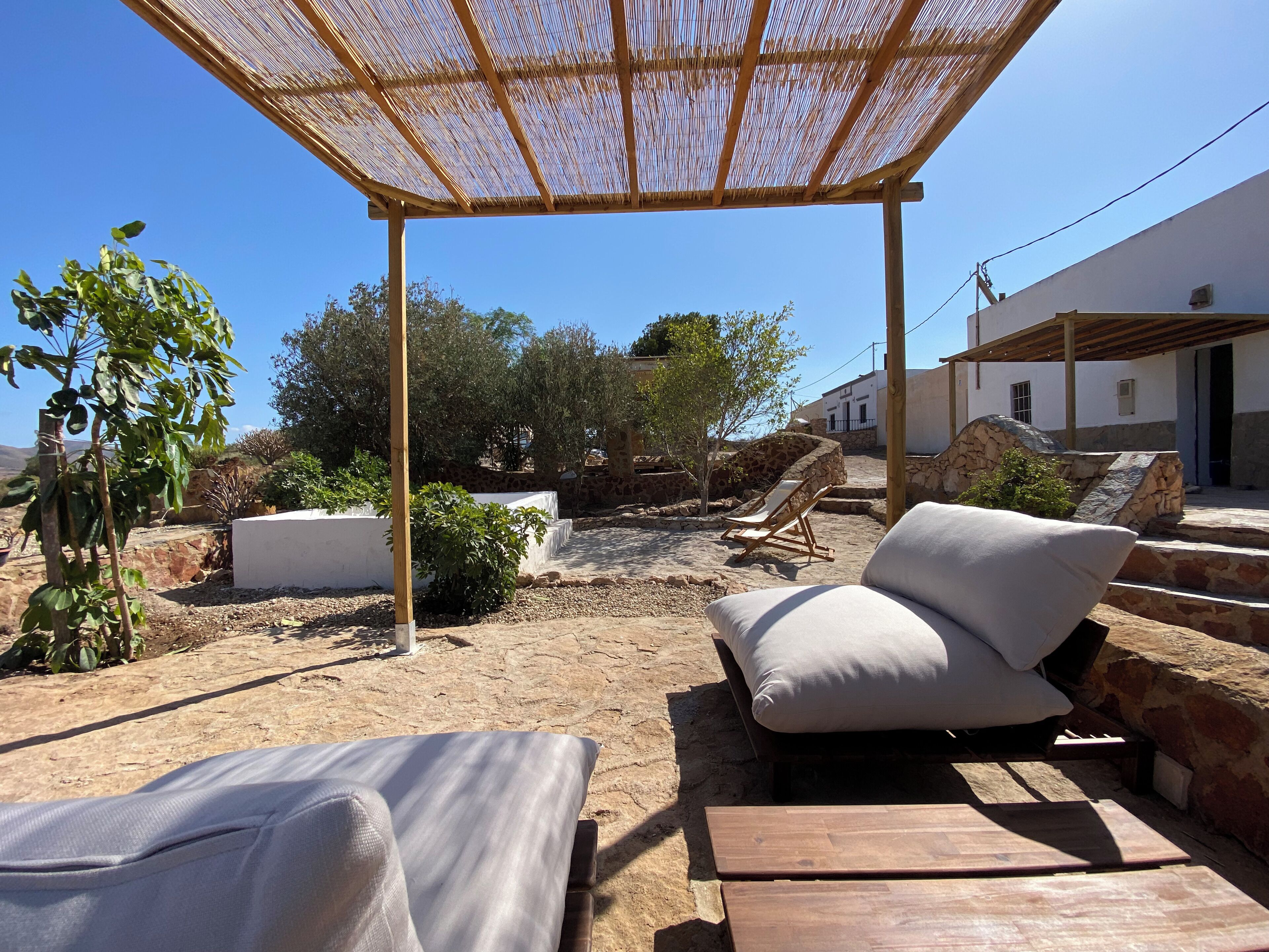 An outdoor seating area with a pergola, lounge chairs, and a stone wall.
