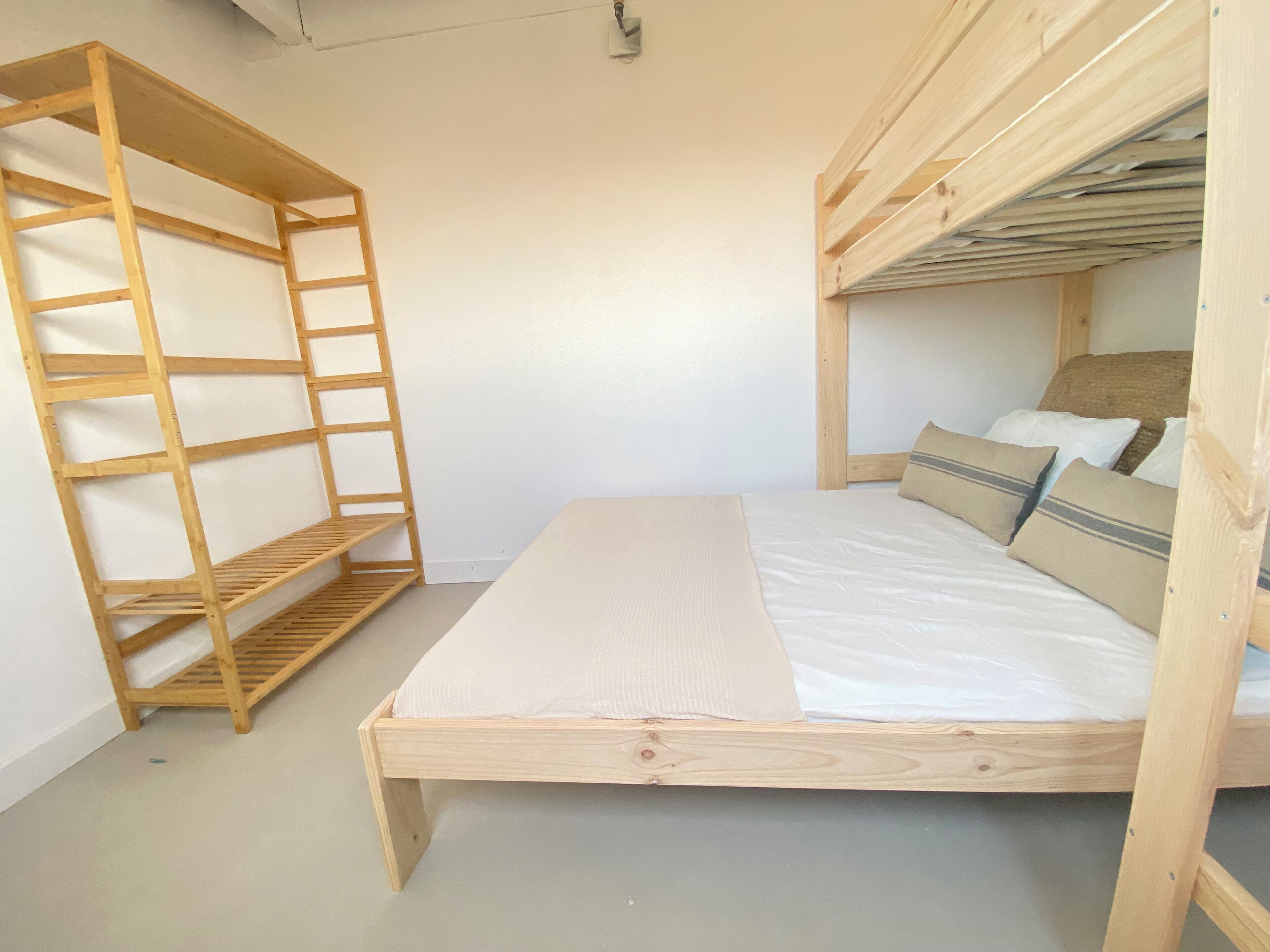 A bunk bed with a wooden ladder and a shelf unit beside it.