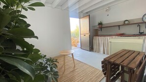 A room with a wooden table, a small stool, a large potted plant, a kitchen area with a sink and a shelf, and a door leading outside. - Casa Lola - Rural apartment with private swimming pool in Cabo de Gata (AN)