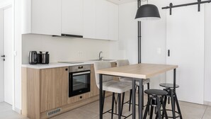 Una cucina moderna con mobili bianchi, un'isola in legno, una lampada a sospensione nera e un'area pranzo con sgabelli.