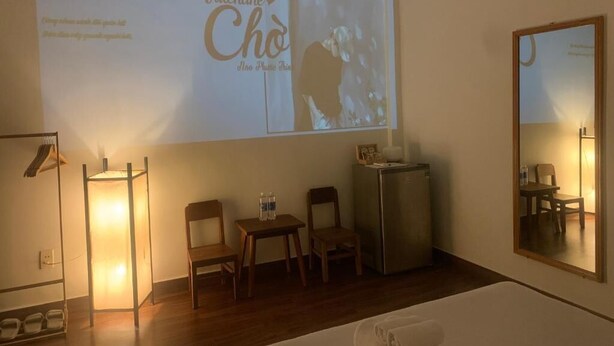 A hotel room with a bed, a desk, two chairs, a small table with water bottles, a refrigerator, and a large screen displaying a Valentine's Day message. - The Hideaway Alley Bui Vien (Ho Chi Minh City)