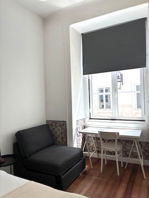 A room with a sofa, a small table, a chair, a window with a view of buildings, and patterned wall tiles. - SJ1D Warm & Inviting | Historic Stay! | A/C (Lisboa ciudad)