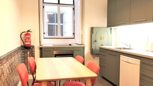 A compact kitchen with a dining table and chairs, a window with bars, and a fire extinguisher. - SJ1D Warm & Inviting | Historic Stay! | A/C (Lisboa ciudad)