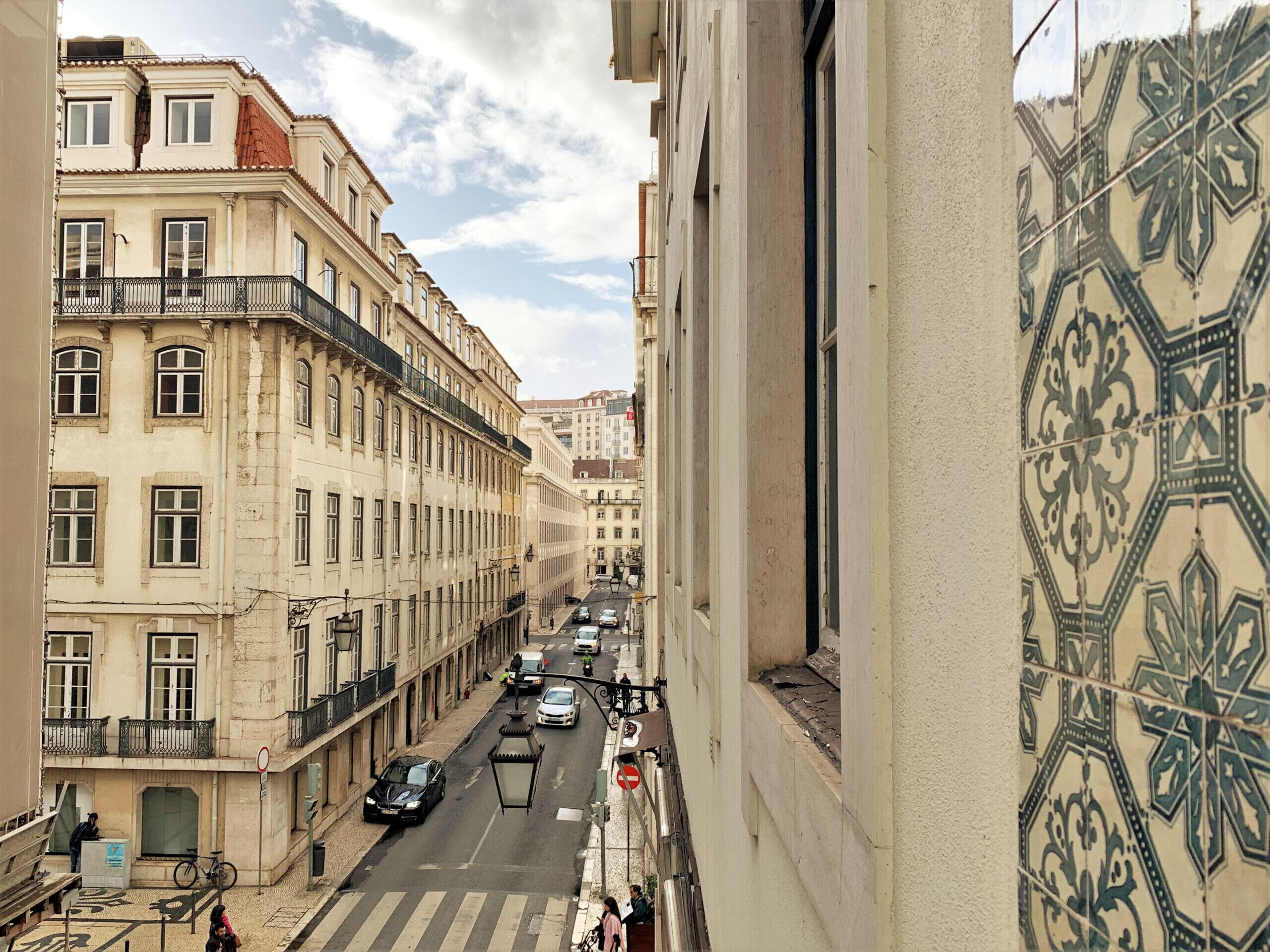 A street view with buildings, cars, and a pedestrian crossing.