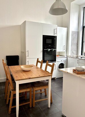 A modern kitchen with white cabinetry, a wooden dining table, and a built-in oven. - SJ2D Newly Renovated! Cosy & Downtown! | Historic Stay! (Lisboa ciudad)