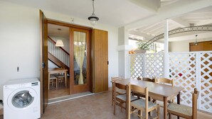 A laundry area with a washing machine, a wooden dining table with chairs, and a staircase leading to an upper level. - Apartment 'Borgo Stella X' with Private Terrace, Wi-Fi and Air Conditioning (Bibione)