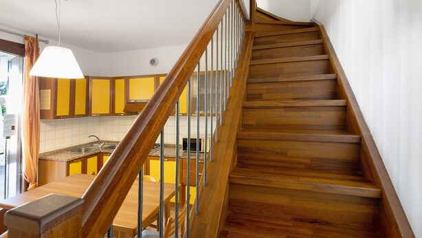 A wooden staircase leading to a kitchen with yellow cabinets and a dining area. - Apartment 'Borgo Stella X' with Private Terrace, Wi-Fi and Air Conditioning (Bibione)