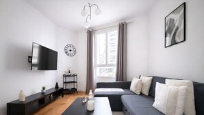 Un salon moderne avec un téléviseur à écran plat, une table basse noire, un canapé gris et une table d’appoint noire.