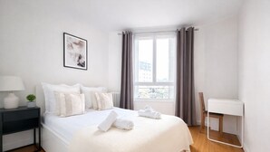 Ein ordentlich eingerichtetes Schlafzimmer mit Bett, Nachttisch, Stuhl und einem Fenster mit Vorhängen.