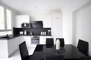 Una cocina moderna con armarios blancos, encimera negra y un comedor con mesa y sillas negras.