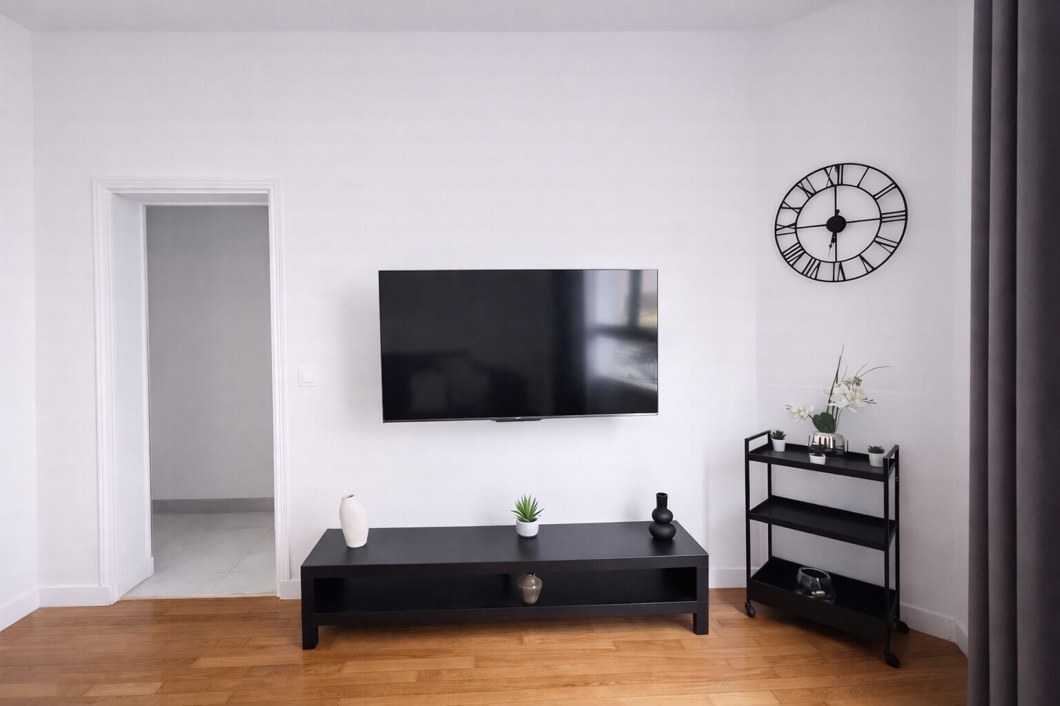 Una sala de estar moderna con un televisor de pantalla plana montado en la pared, un mueble de entretenimiento negro debajo y un reloj minimalista en la pared.