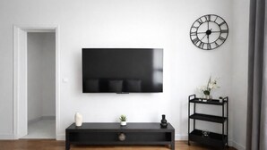 Un salon moderne avec un téléviseur à écran plat fixé au mur, un meuble de rangement noir agrémenté d’une plante, d’un vase et d’une petite étagère.