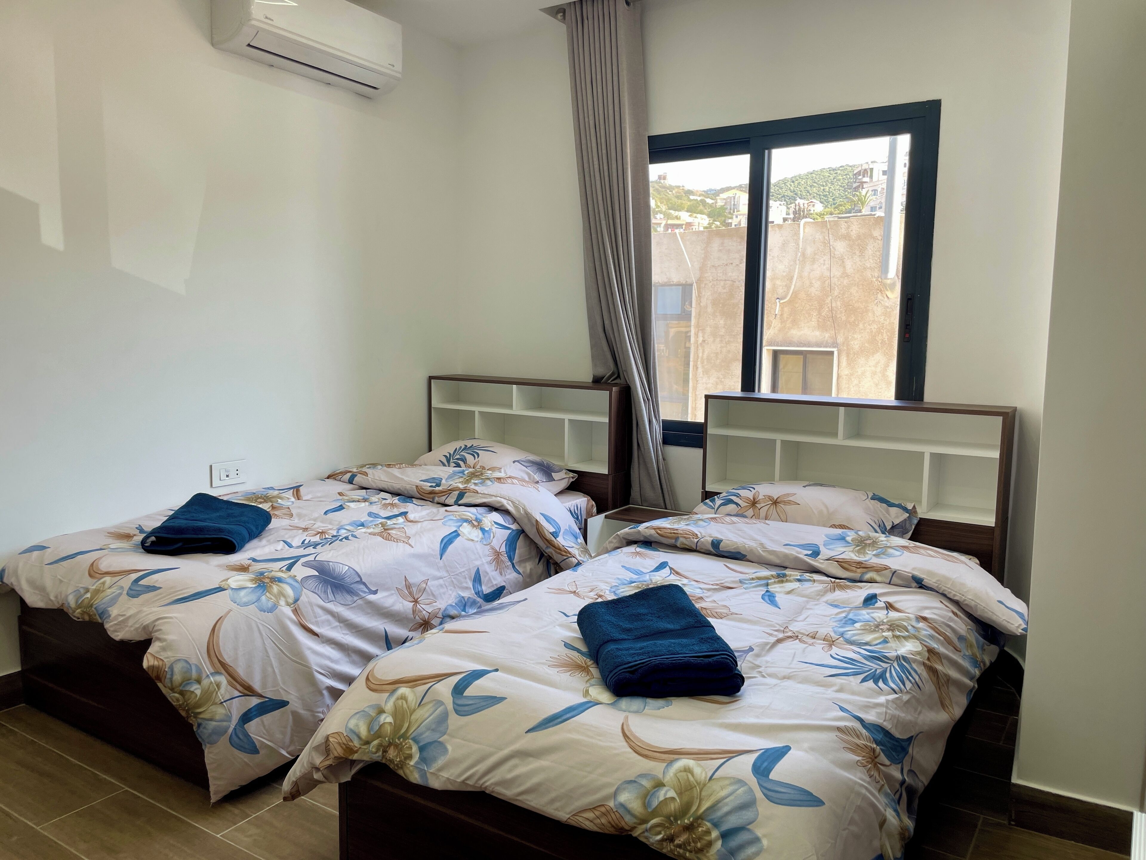 Una camera d'albergo con due letti, ognuno con una coperta a fiori e un asciugamano blu.