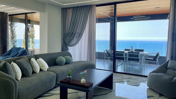 A modern living room with a grey sofa, a coffee table, and a balcony with a view of the sea. - Kfaraabida SKY (Batroun)