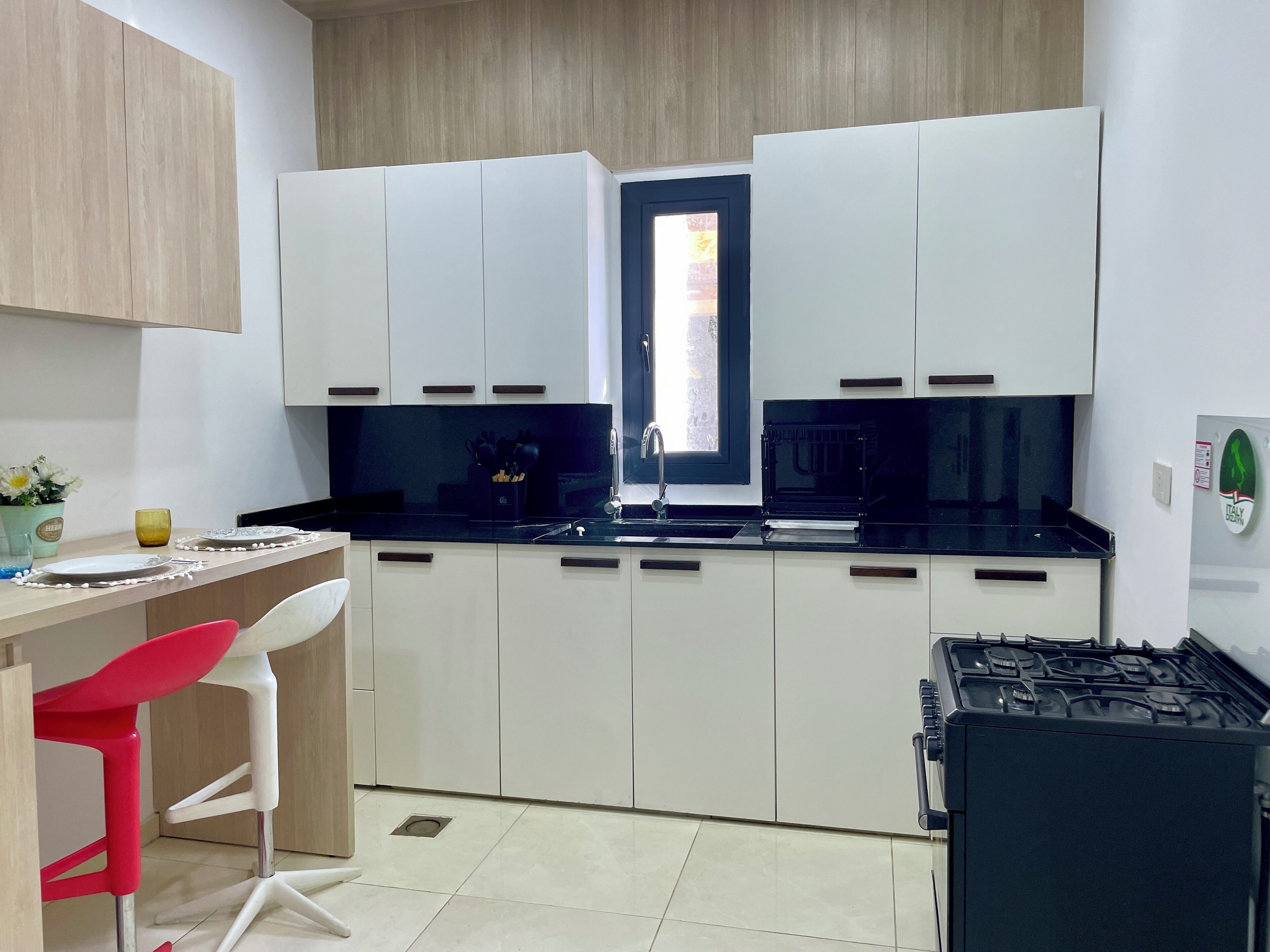 A compact kitchen with white cabinets, a black countertop, a red chair, and a gas stove.