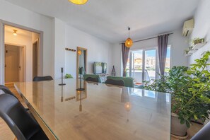 A modern living room with a glass dining table, comfortable seating, a TV, and a balcony with plants. - Family house with patio - Los Lances beach area (Tarifa)