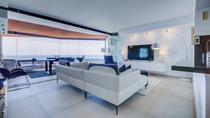 Una sala de estar moderna con un sofá blanco, un televisor y un comedor con sillas y una mesa.