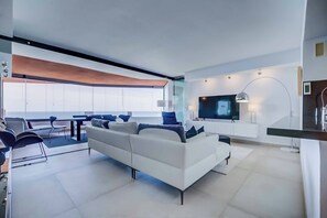 A modern living room with a white sofa, a TV, and a dining area with chairs and a table. - 28 - Exclusive Modern Penthouse with Stunning Views & Pool, Benalmadena (Benalmádena)