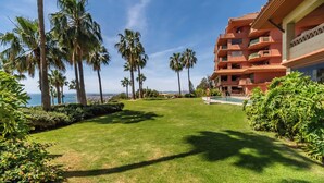 Un césped cuidado con palmeras, un edificio con balcones y una vista despejada del océano.