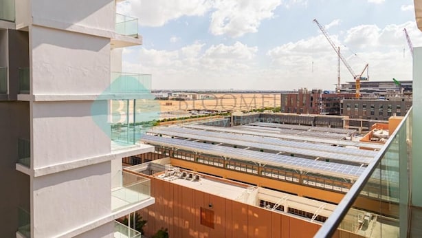 A modern building with multiple floors, large windows, and a construction site in the background. - Bloomfields Iconic 1BR in Oasis Masd (Abu Dhabi)