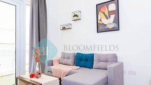 A modern living room with a grey sofa, a small table with a vase, and a framed abstract painting on the wall. - Bloomfields Iconic 1BR in Oasis Masd (Abu Dhabi)