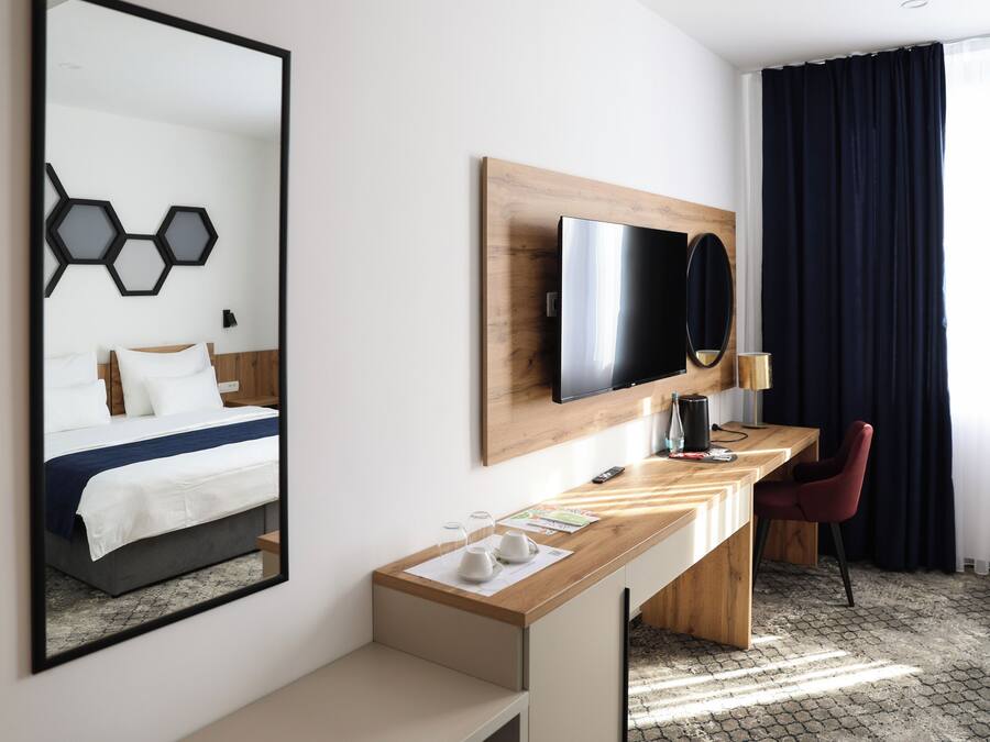 A hotel room with a bed, a desk, a chair, a TV, and a large mirror.