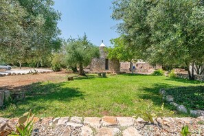 A courtyard with a stone building, surrounded by trees and a grassy area. - Casa di Paolo by Rentbeat (Ceglie Messapica)