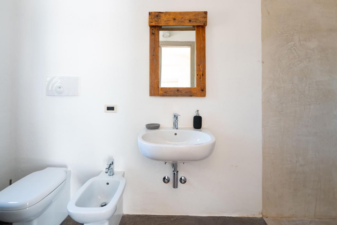 Ein Badezimmer mit Toilette, Bidet und Waschbecken mit einem eckigen Spiegel darüber.