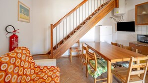 Un espace repas avec une table et des chaises en bois, un escalier, un extincteur et un téléviseur.