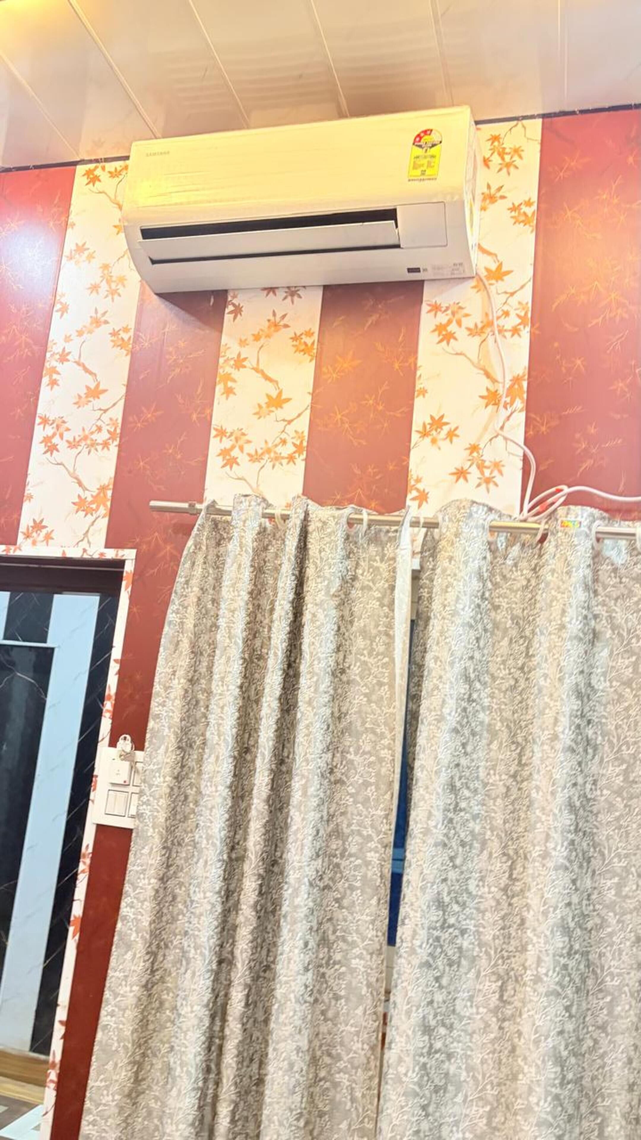 A room with a patterned curtain, a wall-mounted air conditioner, and a door with a red and white design.