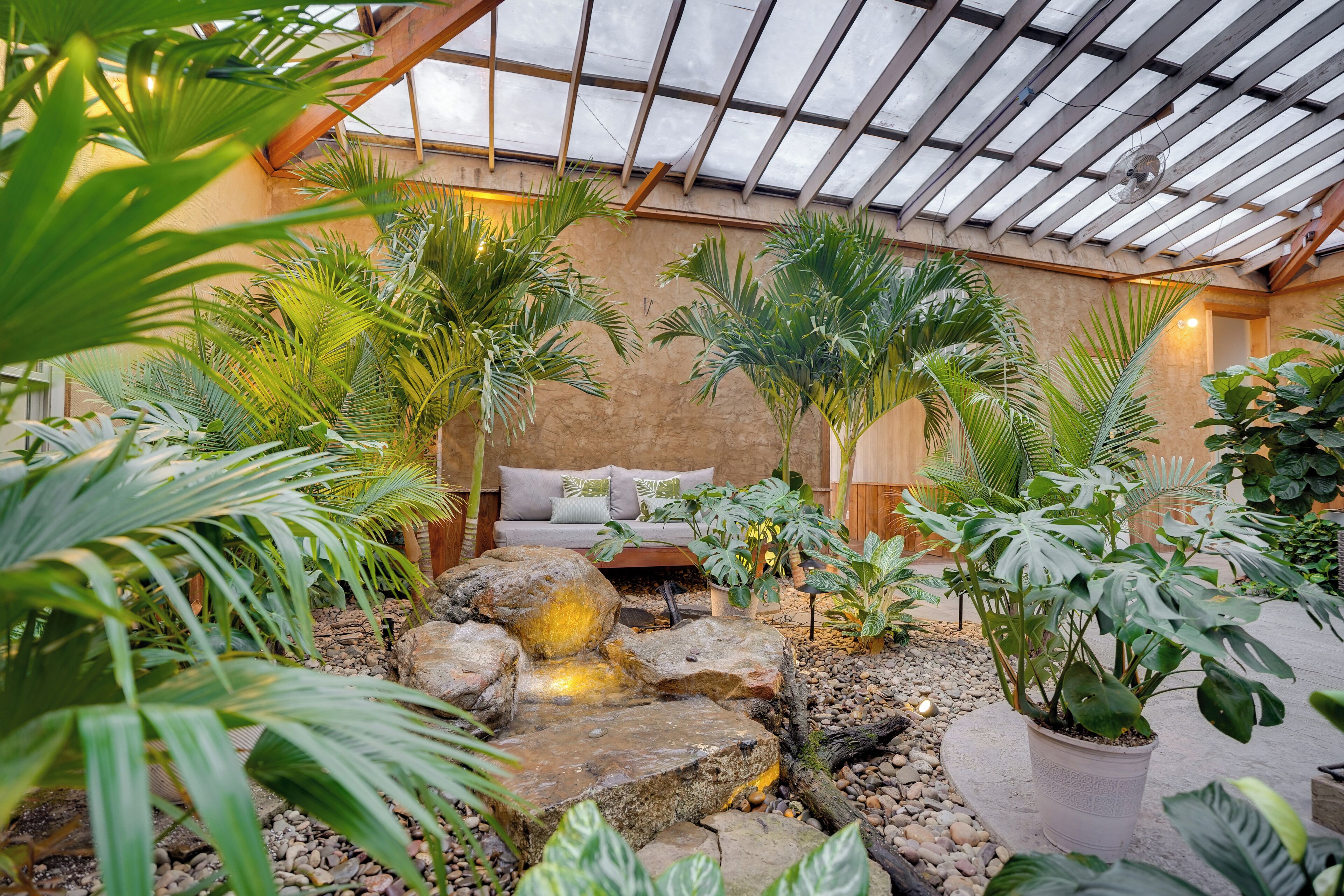 A greenhouse with a wooden bench, potted plants, and a small water feature.