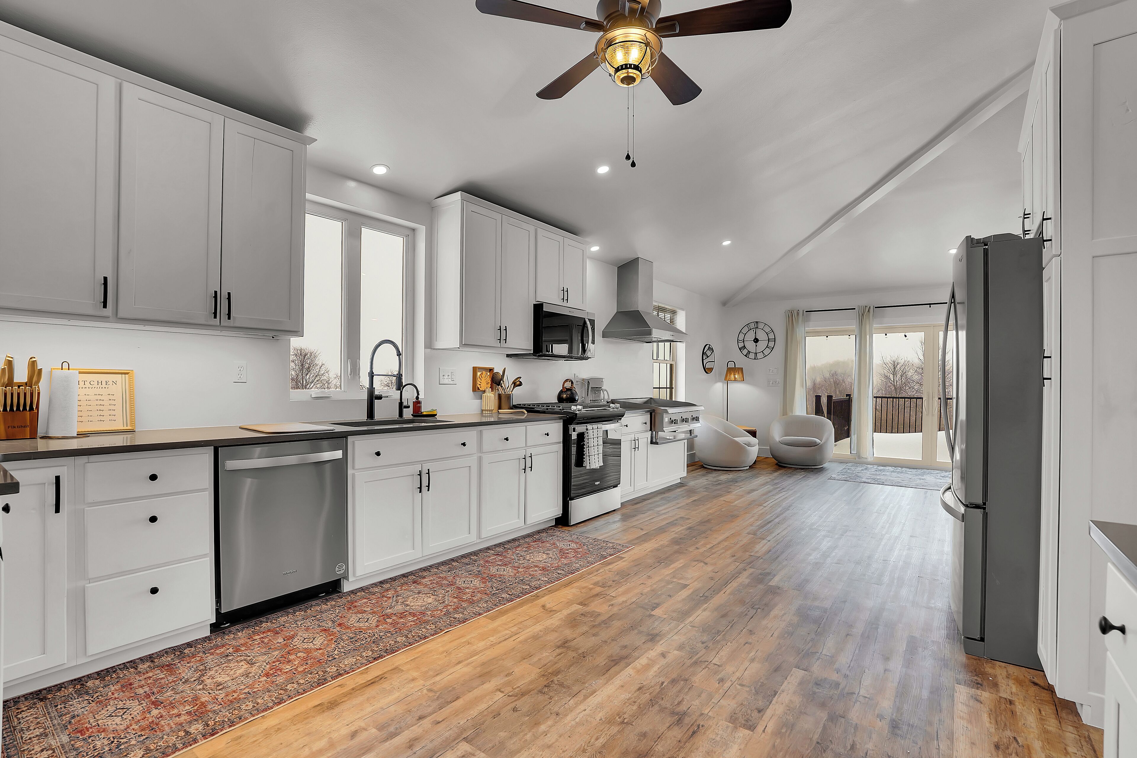 A spacious kitchen with white cabinets, a dishwasher, a stove, and a ceiling fan.