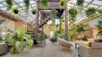 A spacious atrium with hanging plants, a central staircase, and wicker furniture.